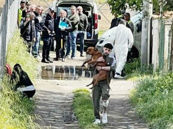Lo zio del bambino sbranato dai pitbull porta in braccio uno dei cani: sullo sfondo tecnici, forze dell'ordine e presenti alla tragedia